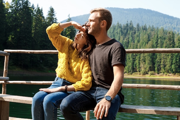 Joven pareja hermosa sonriendo, abrazándose, disfrutando del paisaje de las montañas