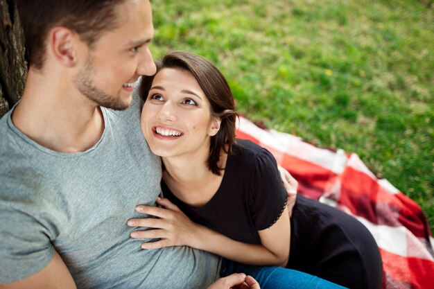 Joven pareja hermosa sonriendo, descansando en un picnic en el parque.