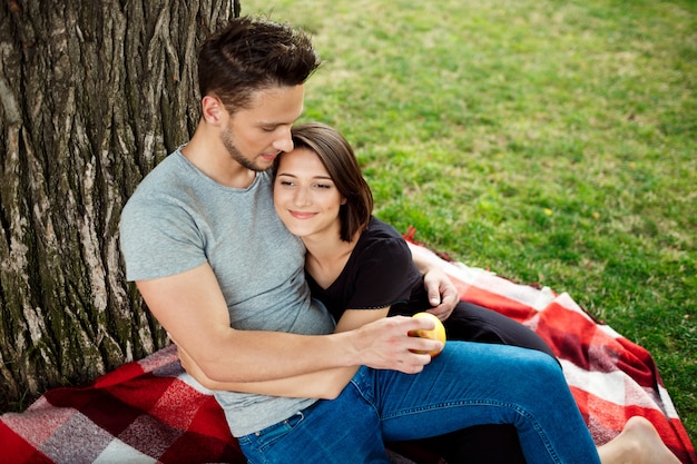 Joven pareja hermosa sonriendo, descansando en un picnic en el parque.