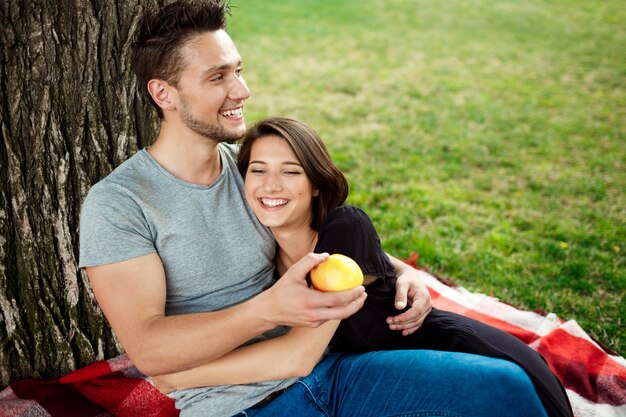 Joven pareja hermosa sonriendo, descansando en un picnic en el parque.