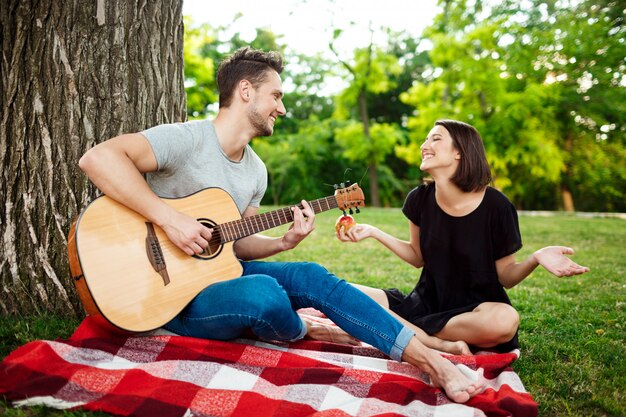 Joven pareja hermosa sonriendo, descansando en un picnic en el parque.