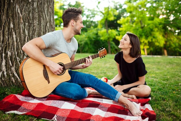 Joven pareja hermosa sonriendo, descansando en un picnic en el parque.