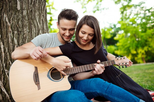 Joven pareja hermosa sonriendo, descansando en un picnic en el parque.