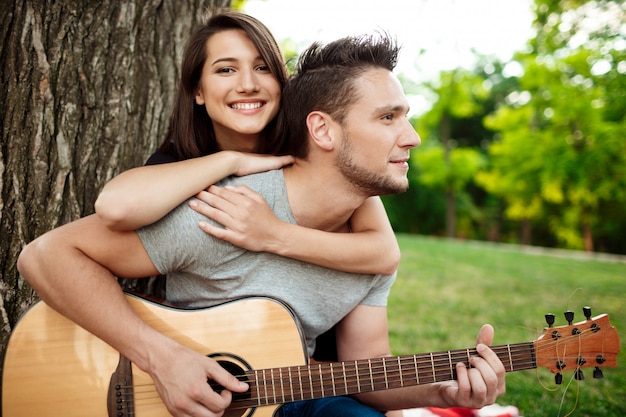 Joven pareja hermosa sonriendo, descansando en un picnic en el parque.