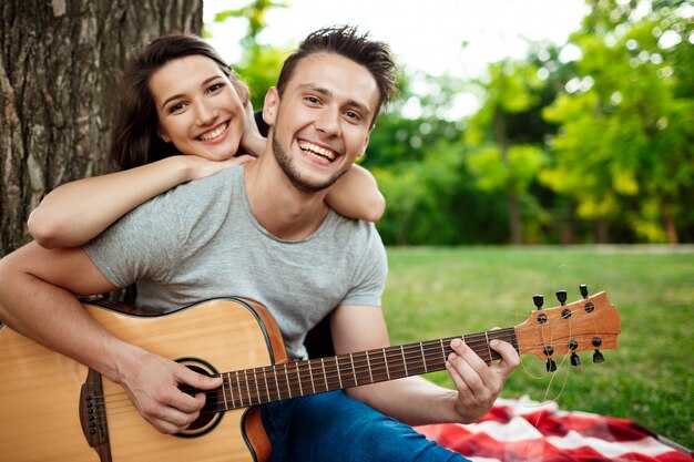 Joven pareja hermosa sonriendo, descansando en un picnic en el parque.