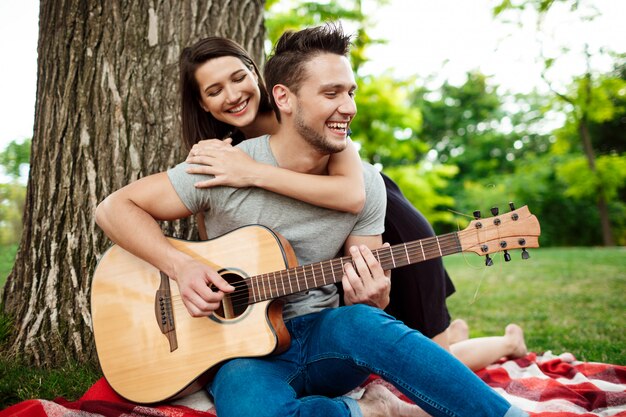 Joven pareja hermosa sonriendo, descansando en un picnic en el parque.