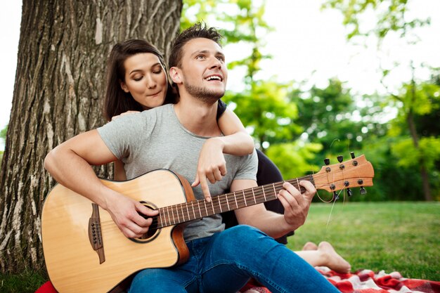 Joven pareja hermosa sonriendo, descansando en un picnic en el parque.