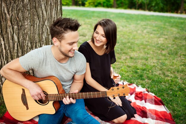 Joven pareja hermosa sonriendo, descansando en un picnic en el parque.