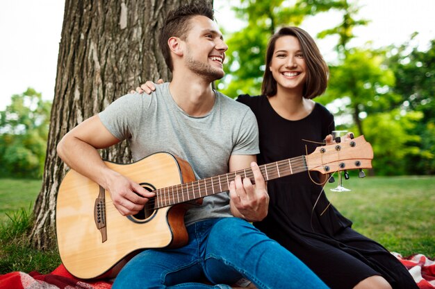 Joven pareja hermosa sonriendo, descansando en un picnic en el parque.