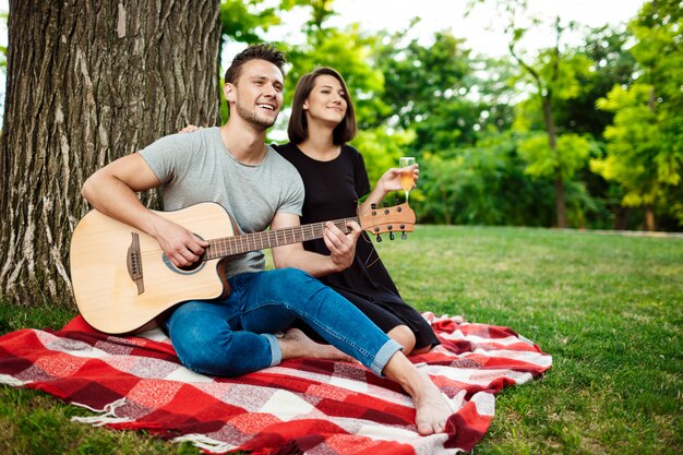 Joven pareja hermosa sonriendo, descansando en un picnic en el parque.