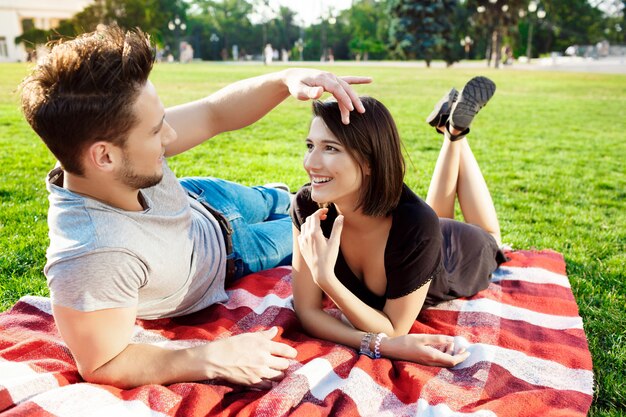 Joven pareja hermosa sonriendo, descansando en un picnic en el parque.