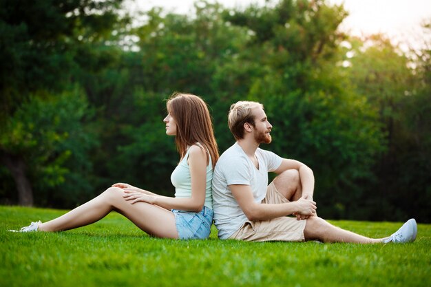 Joven pareja hermosa sonriendo, sentado en el césped en el parque.