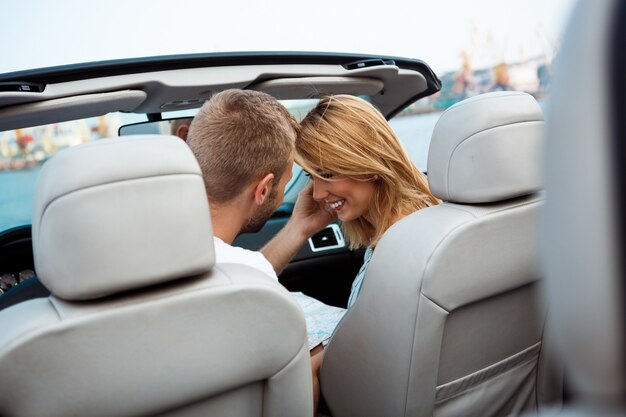 Joven pareja hermosa sonriendo, sentado en el coche cerca del mar.