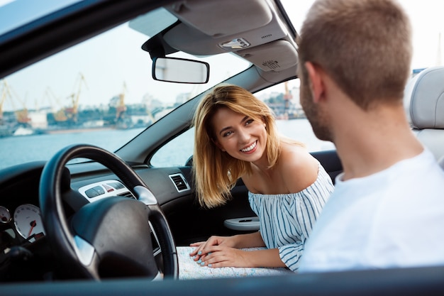 Joven pareja hermosa sonriendo, sentado en el coche cerca del mar.