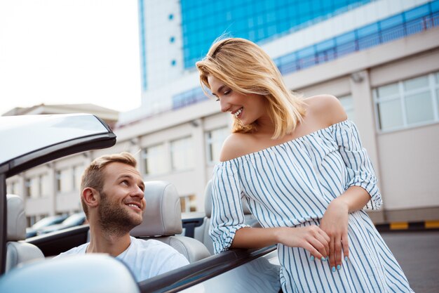 Joven pareja hermosa sonriendo, sentado en el coche cerca del mar.