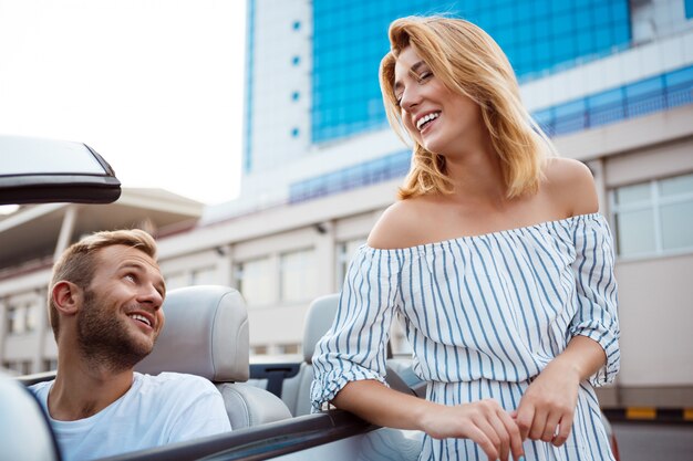 Joven pareja hermosa sonriendo, sentado en el coche cerca del mar.