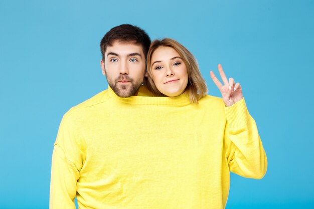 Joven pareja hermosa en un suéter amarillo posando sobre pared azul