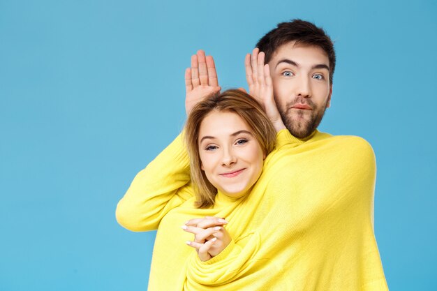 Joven pareja hermosa en un suéter amarillo posando sonriendo divirtiéndose sobre pared azul