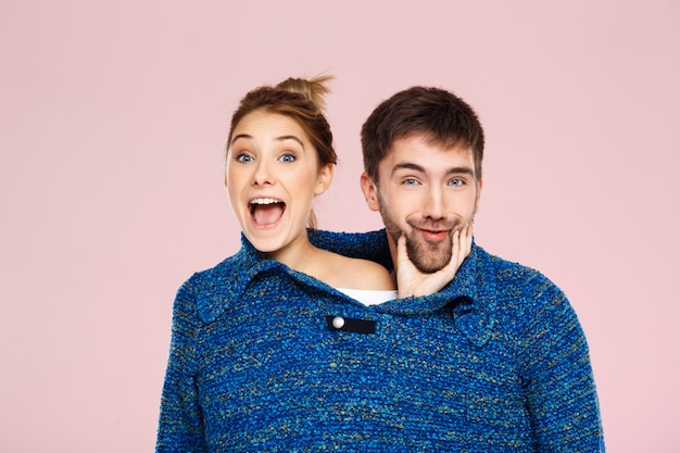 Joven pareja hermosa en un suéter de punto azul posando sonriendo divirtiéndose sobre pared rosa claro