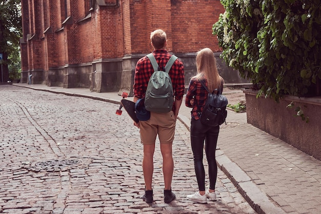 Joven pareja hipster, guapo patinador y su novia caminando por las viejas calles de Europa.