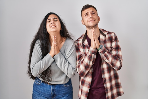 Foto gratuita joven pareja hispana de pie sobre fondo blanco rogando y rezando con las manos juntas con expresión de esperanza en la cara muy emocional y preocupada rogando