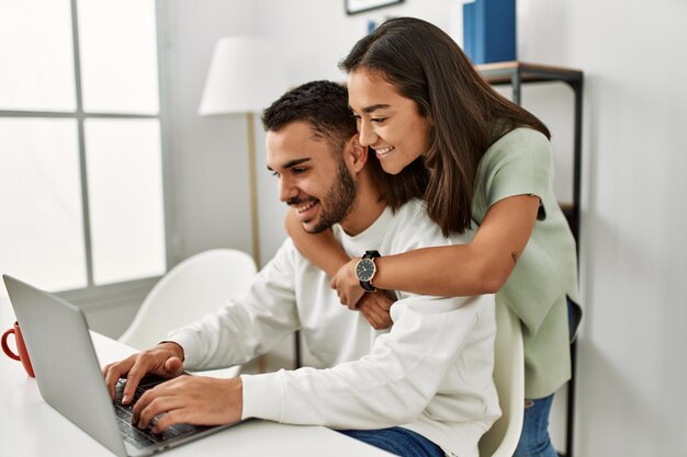 Joven pareja latina usando laptop y tomando café en casa.