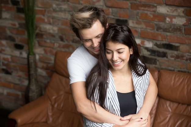 Joven pareja milenaria abrazada en casa, feliz por el primer embarazo