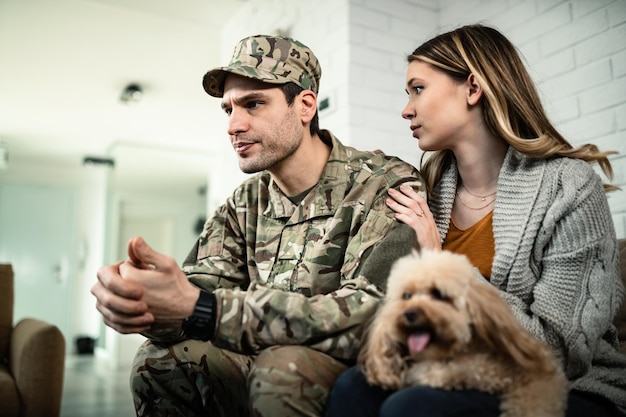 Joven pareja militar angustiada con un perro en casa La mujer está consolando a su esposo mientras él está a punto de irse para el despliegue