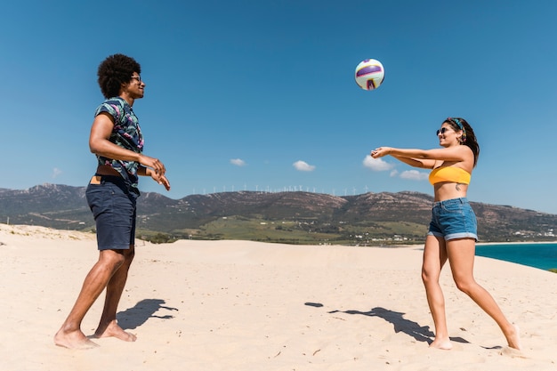 Joven pareja multirracial jugando juego con pelota en la playa