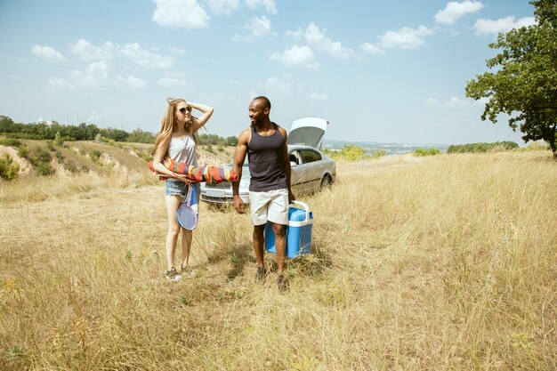 Joven pareja romántica internacional multiétnica al aire libre en la pradera en un día soleado de verano. Hombre afroamericano y mujer caucásica haciendo picnic juntos. Concepto de relación, verano.