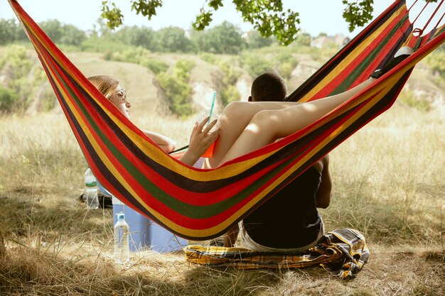 Joven pareja romántica internacional multiétnica al aire libre en la pradera en un día soleado de verano. Hombre afroamericano y mujer caucásica haciendo picnic juntos. Concepto de relación, verano.