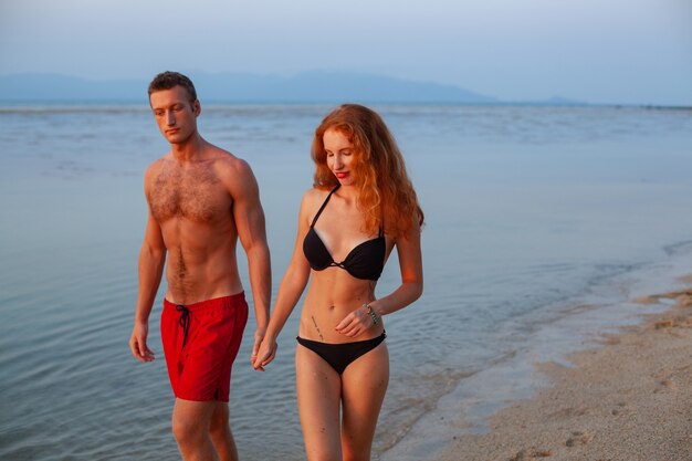 Joven pareja romántica sexy enamorada feliz en la playa de verano juntos divirtiéndose vistiendo trajes de baño