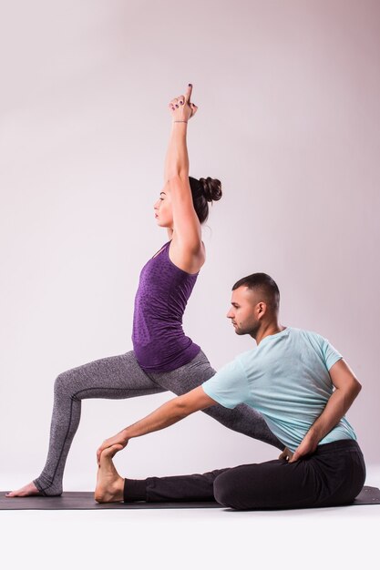 Joven pareja sana hombre y mujer en posición de yoga sobre fondo blanco.