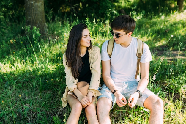 Joven pareja sentada en la hierba verde mirando el uno al otro