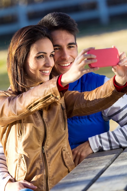 Joven pareja tomando fotos con teléfonos inteligentes en el parque