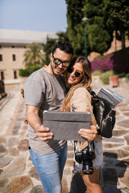 Joven pareja de turistas en gira tomando selfie en tableta digital