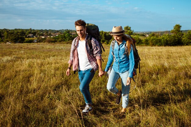 Joven pareja de viajeros con mochilas sonriendo, caminando en el campo