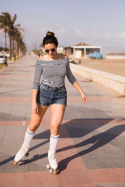 Joven patinador femenino patinando en la acera cerca de la playa