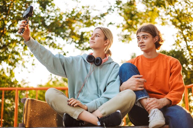 Joven patinador y niña grabando un nuevo video mientras pasan tiempo juntos en el skatepark