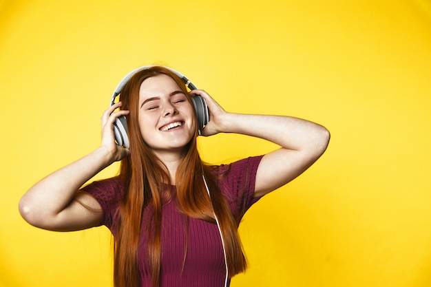 Joven pelirroja es feliz y escucha música a través de auriculares con los ojos cerrados