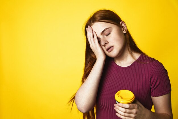 Joven pelirroja está con sueño y sostiene una taza con café de pie