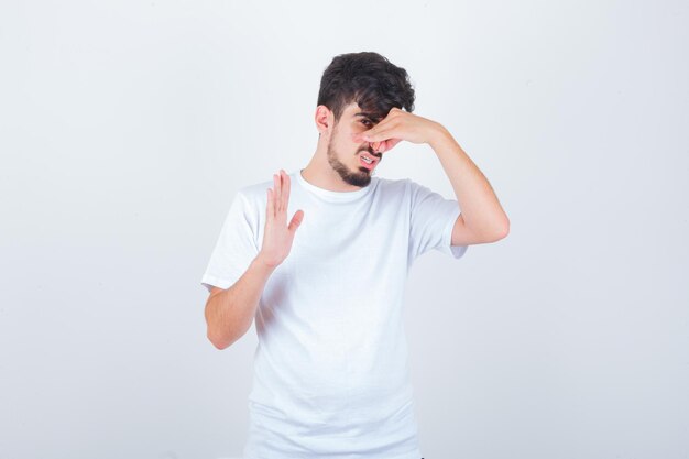 Joven pellizcando la nariz debido al mal olor en la camiseta y mirando disgustado