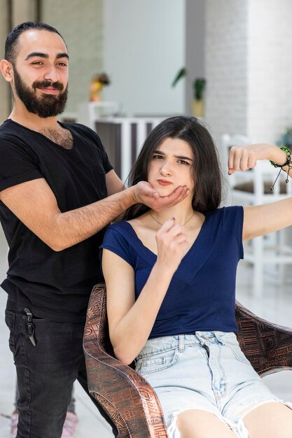 Joven peluquero sosteniendo la barbilla de su cliente y sonriendo Foto de alta calidad