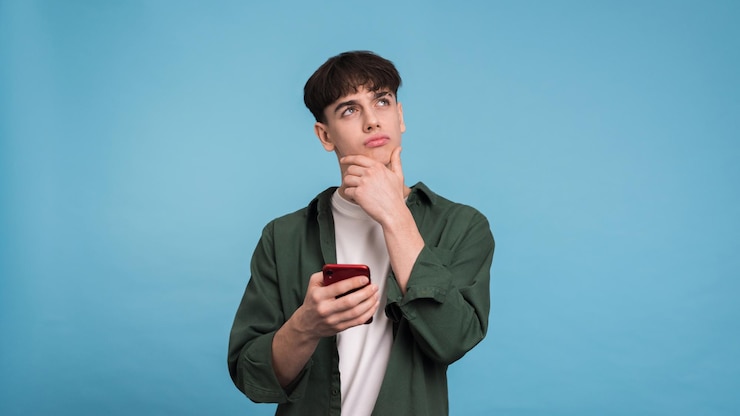 Foto gratuito joven pensante sosteniendo su teléfono
