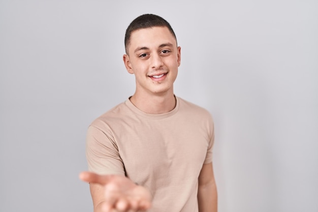 Foto gratuita joven de pie sobre un fondo aislado sonriendo alegre ofreciendo la mano de la palma dando asistencia y aceptación