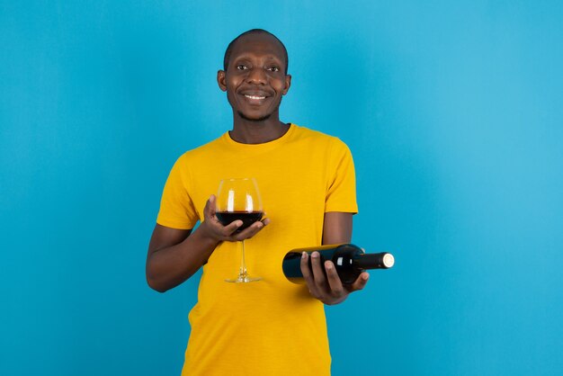 Joven de piel oscura con camisa amarilla con vino tinto en la pared azul