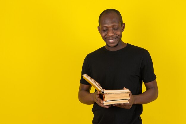 Joven de piel oscura sosteniendo el libro y leyendo en la pared amarilla