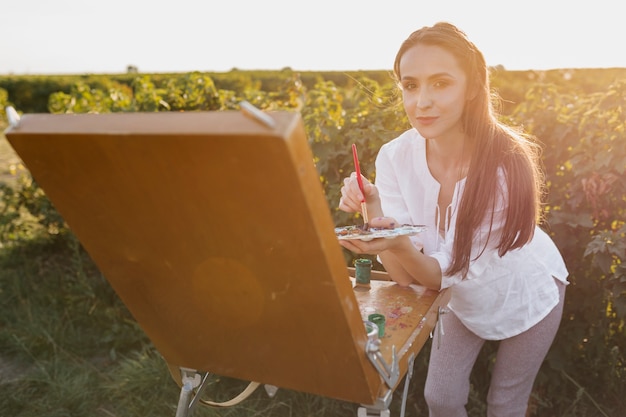 Foto gratuita joven pintor en la naturaleza mirando a cámara