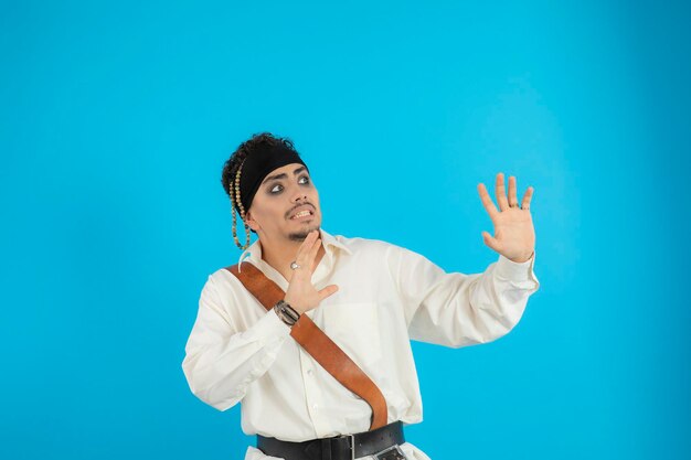 Un joven pirata asustado se para sobre fondo azul y mira a un lado. foto de alta calidad