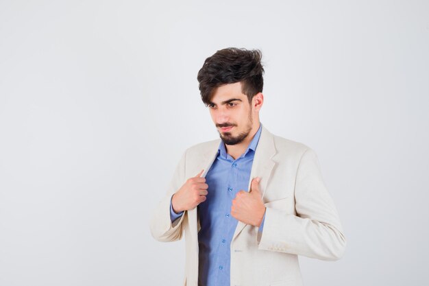 Joven poniendo las manos en la chaqueta con camisa azul y chaqueta de traje blanco y mirando feliz